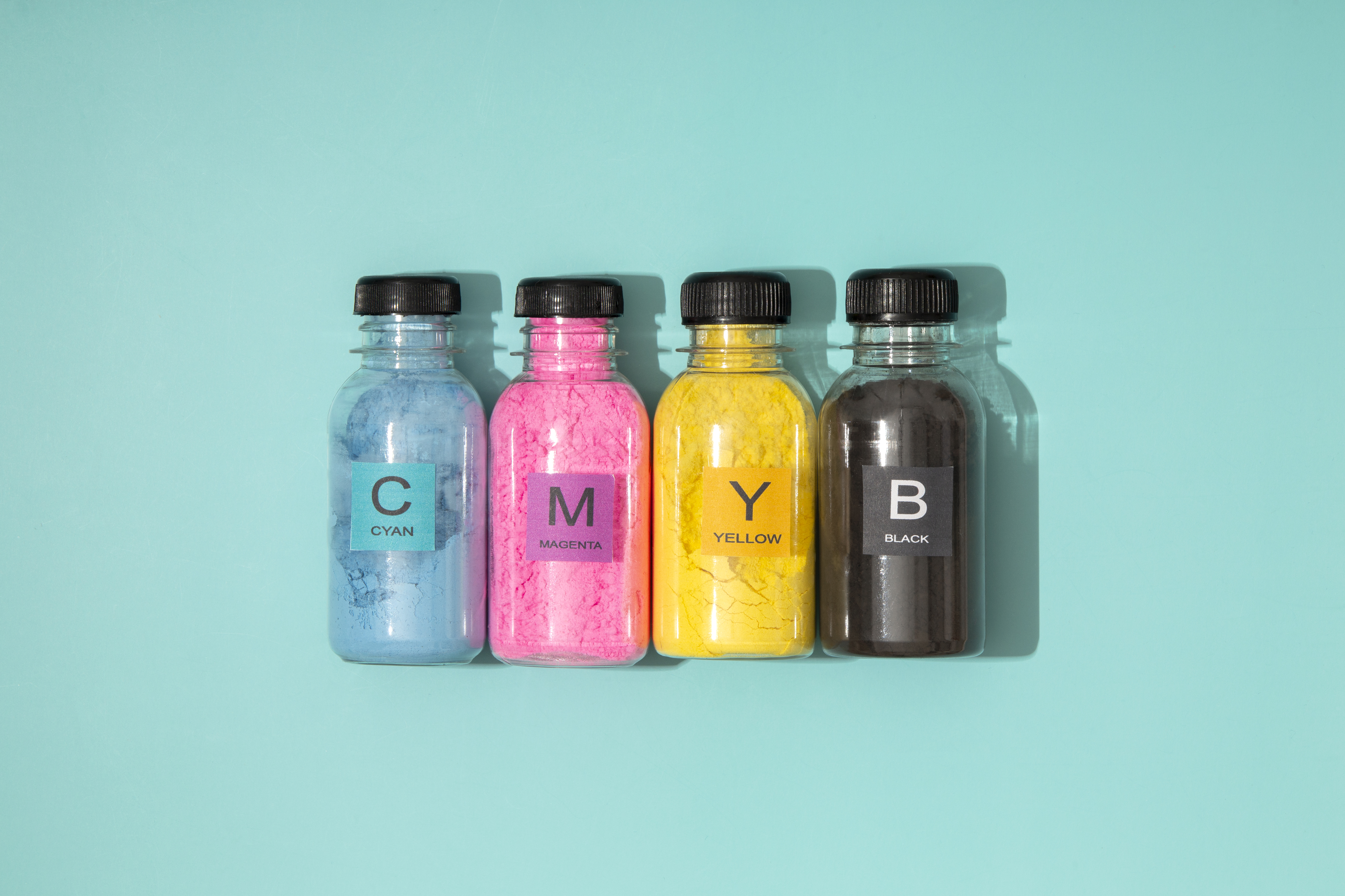 4 bottles with cmyk colours and letter in each bottle on top of a light blue background. 